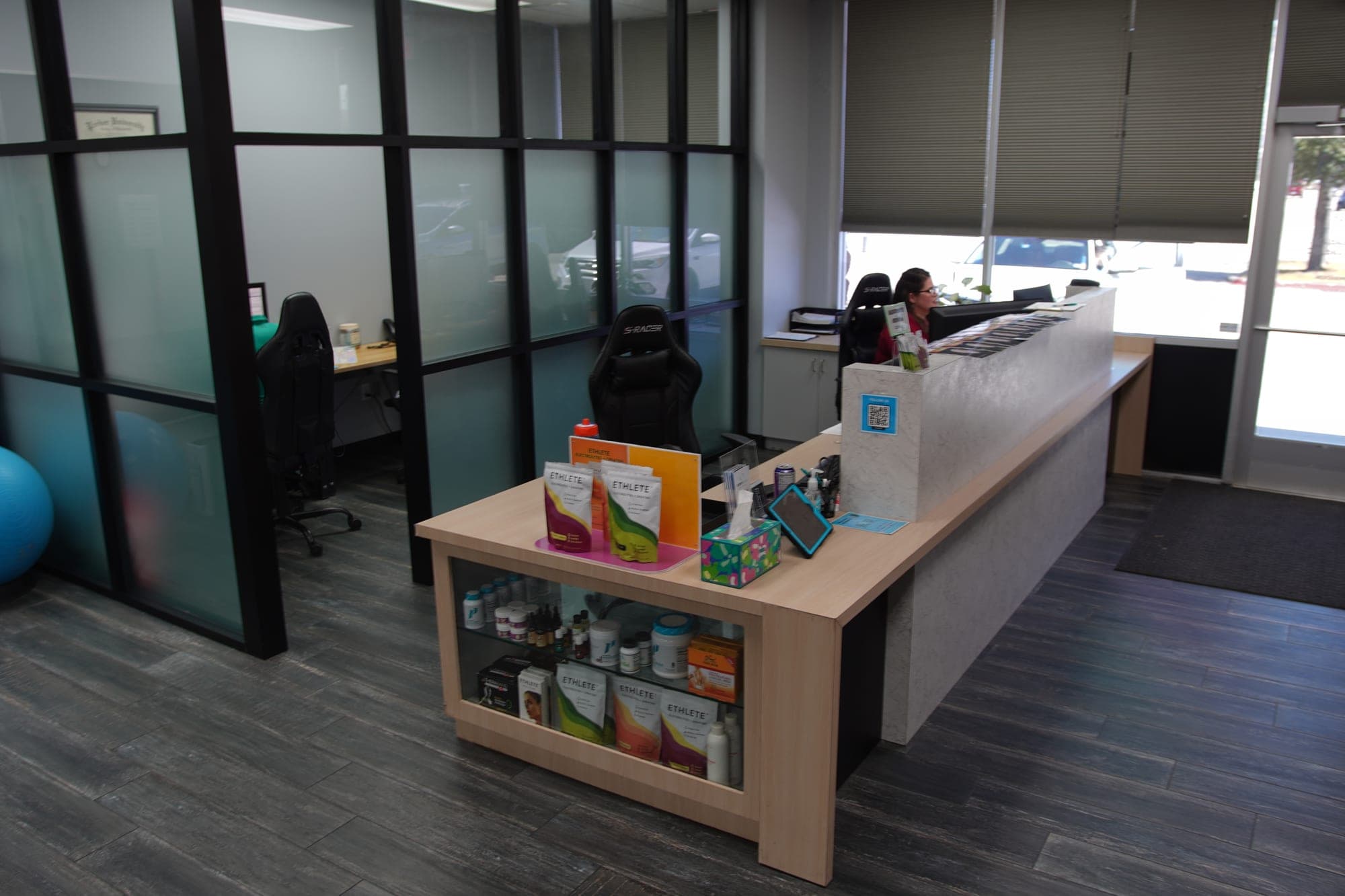 Front desk at Breakaway Chiropractic & Wellness in Frisco with a staff member at the computer, a display of supplements and recovery products, and frosted-glass offices behind