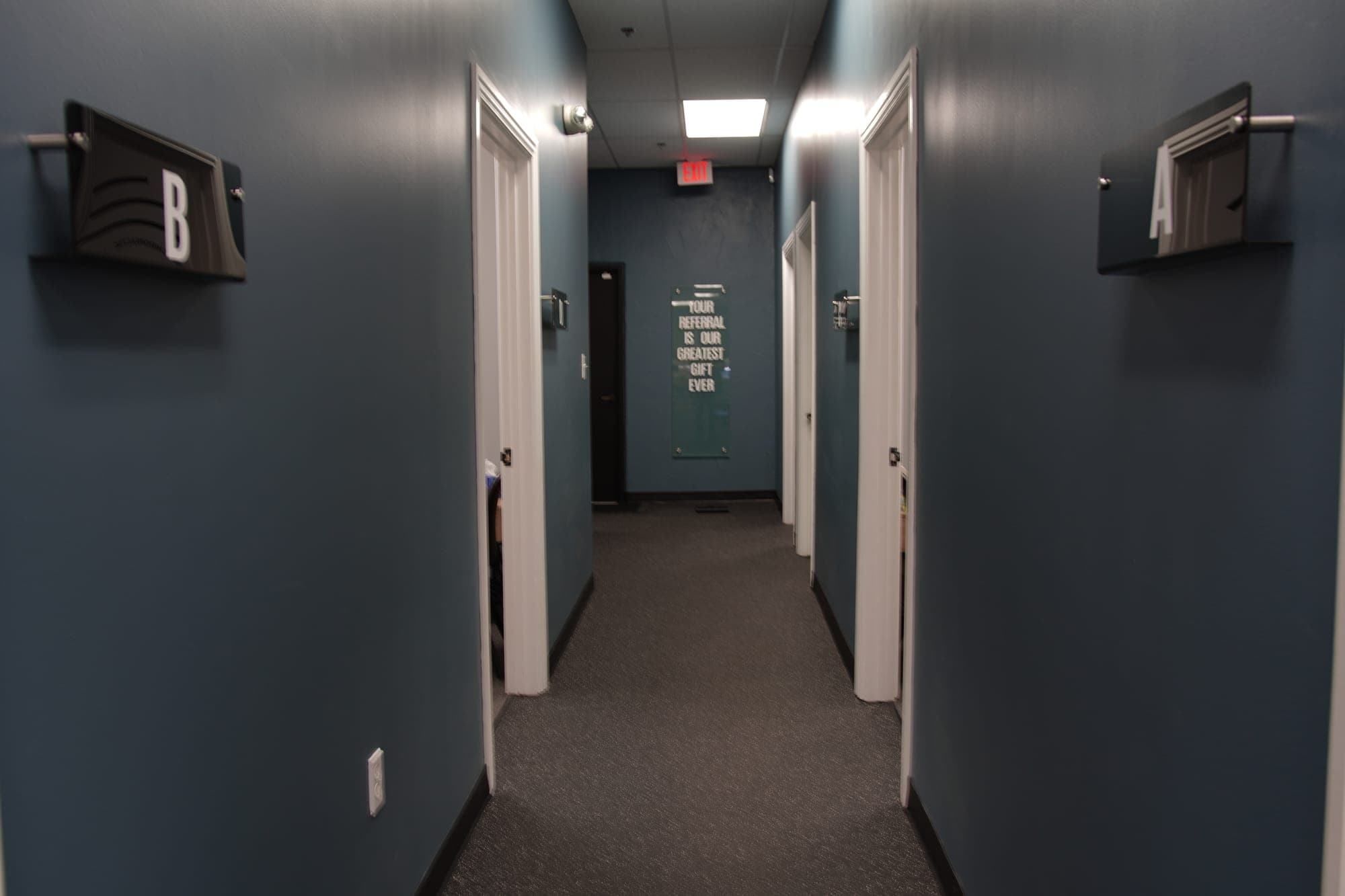 Hallway to the treatment rooms with lettered room signs and a sign reading Your referral is our greatest gift ever